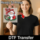 A smiling woman holds InkMerge’s Tis the Season Santa Claus Design DTF transfer sheet—ideal for your next ugly sweater party. An arrow highlights her black shirt with the text: Ready to Press and DTF Transfer.