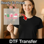 A woman in a black t-shirt holds an InkMerge Tis the Season Festive Design transparent DTF transfer sheet, labeled Ready To Press. Perfect for holiday craft projects and compatible with any heat press.