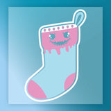 InkMerge’s Quirky Skull Christmas Stocking Design features pastel blue and pink with a mischievous skull face, heart eyes, jagged mouth, and dripping details—ideal for DTF transfers or as an ugly sweater party backdrop.
