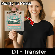 A smiling woman in a black shirt holds the InkMerge Booked Up The Holidays Design - Heat Press Ready transfer, featuring stacked books and festive elements. "Ready To Press" text shows it's perfect for holiday projects.