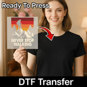 A woman in a black shirt holds an InkMerge Retro Mountain Sunset Design DTF transfer sheet featuring a hiker and NEVER STOP WALKING slogan. An arrow points to her shirt, highlighting this Ready To Press premium heat press transfer.