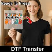 A smiling woman holding a sign with the text "YODELALL mom squad" on it, with a red arrow pointing to her chest.