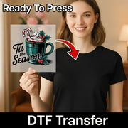 A woman in a black T-shirt holds the InkMerge “Tis the Season Cocoa Design” DTF transfer sheet, featuring a cup, candy canes, and holly. The sheet reads “Ready To Press DTF Transfer” with an arrow showing heat press application.