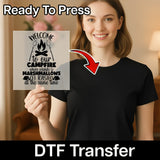 A woman smiles while holding the InkMerge Welcome to Our Campfire Design DTF transfer, featuring campfire graphics, playful text, an arrow, and the words "Ready To Press" for heat press application.
