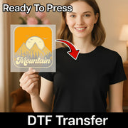 A smiling woman in a black shirt holds a yellow Mountain Sunset Minimalist Landscape DTF transfer by InkMerge. "Ready to Press" is at the top, "Direct-to-Film transfer" at the bottom, with an arrow pointing from the design to her shirt.